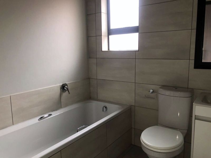 A clean, modern bathroom featuring a built-in bathtub, a toilet, and a vanity unit with neutral wall and floor tiling.