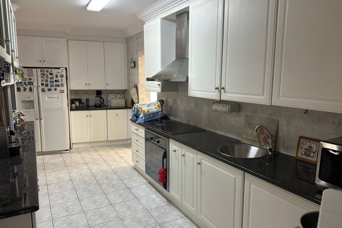 A functional kitchen featuring white cabinetry, dark granite countertops, a stainless steel extractor fan, and a built-in oven with a ceramic hob.