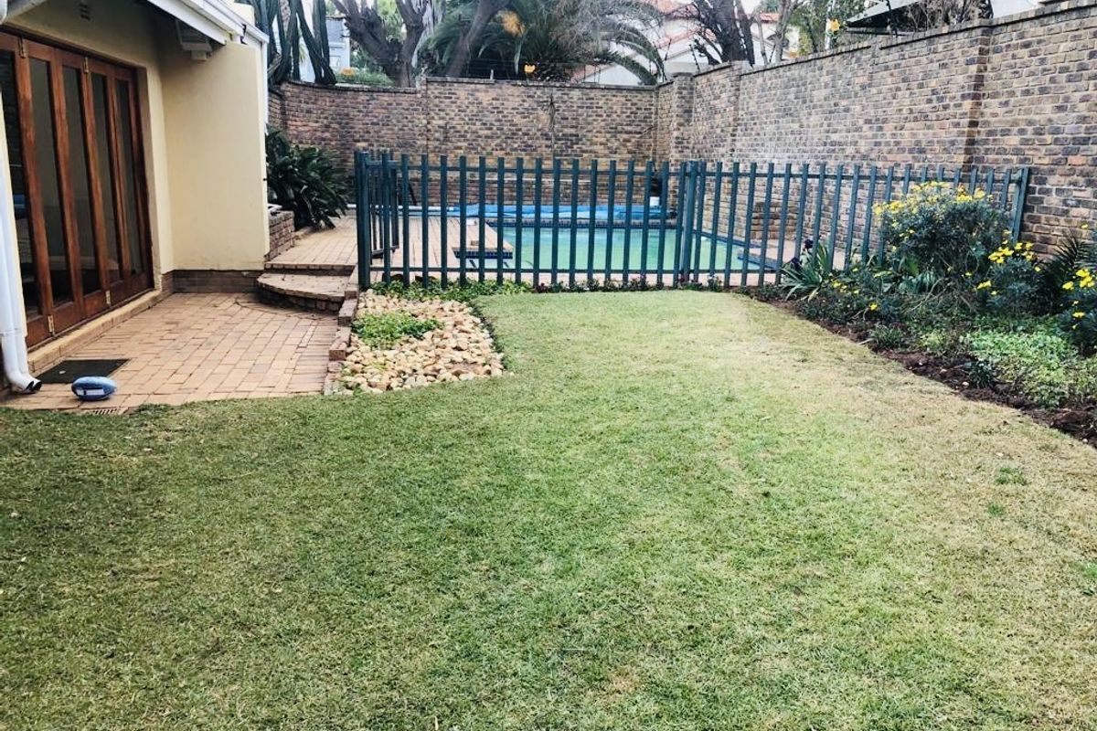 A private rear garden featuring a paved patio area, a fenced swimming pool, and established garden beds with a brick boundary wall.