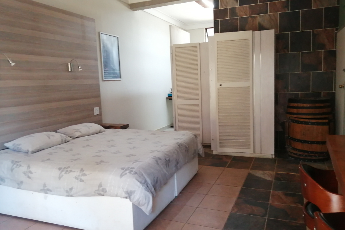 A bedroom featuring a wood-paneled headboard wall, tiled flooring, and built-in louvered closet doors.