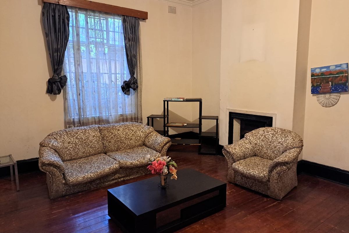 A living room featuring original timber flooring, a fireplace, and a large window with decorative pelmet.