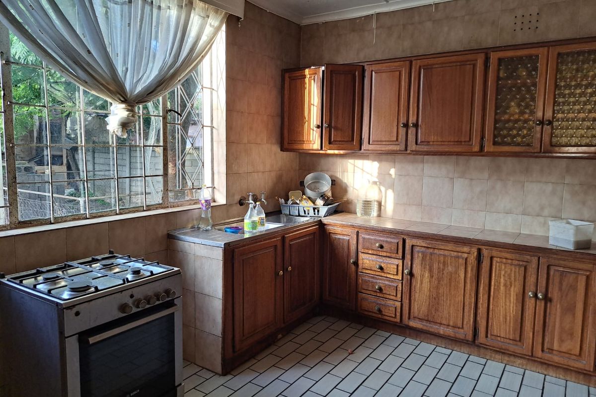 A dated kitchen featuring traditional wooden cabinetry, tiled walls, and a freestanding gas stove, offering a functional layout with potential for modernization.