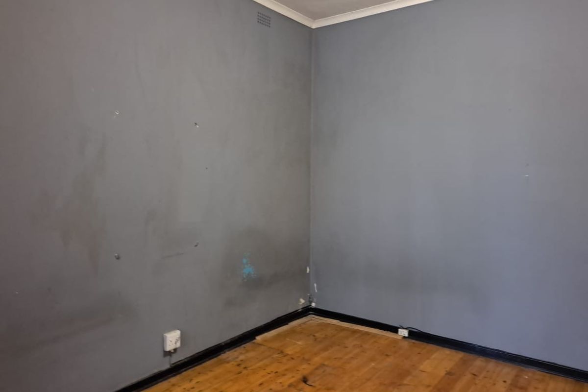 An empty bedroom featuring timber flooring and dark grey painted walls with visible surface wear and scuffing.