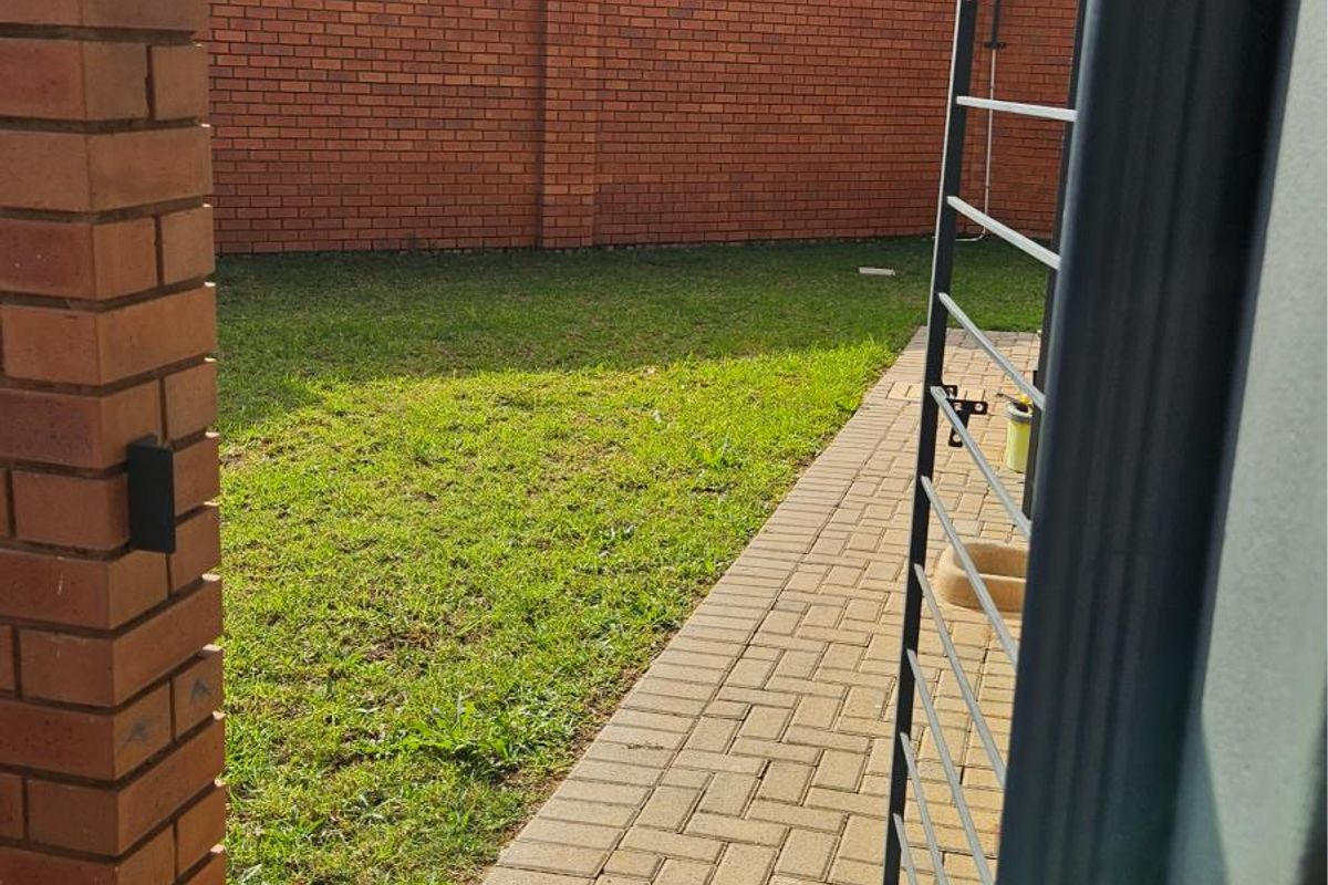 A private rear garden featuring a brick-paved walkway, a brick boundary wall, and a small lawn area.