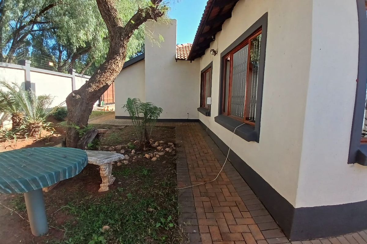 A view of the rear exterior of the house featuring a paved walkway, established garden area, and a brick chimney stack.
