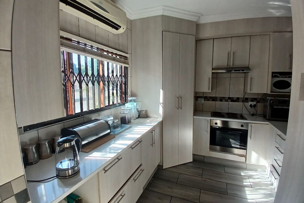 A functional kitchen featuring light-toned cabinetry, built-in oven, hob, extractor fan, and tiled flooring with a security gate on the window.