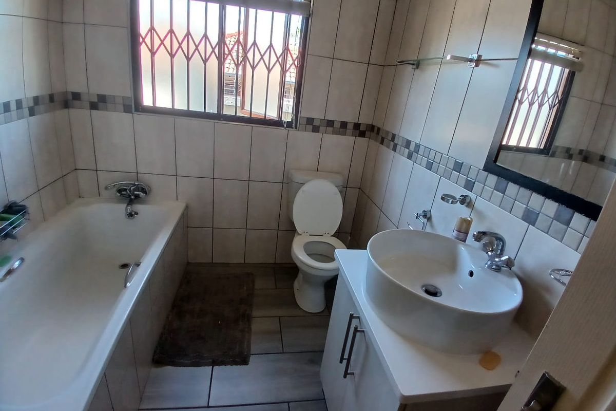 A functional bathroom featuring a bathtub, a modern vessel sink vanity, and a toilet, finished with neutral wall tiles and security bars on the window.