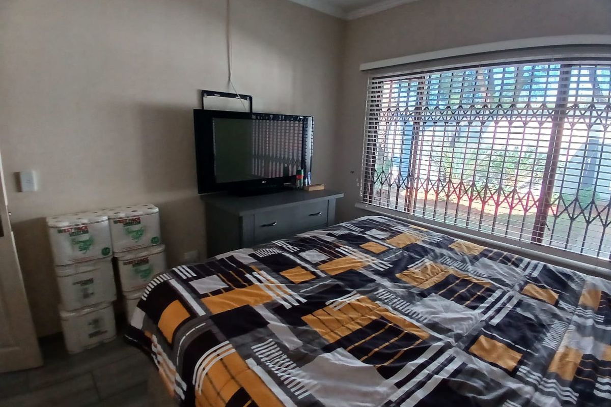 A bedroom featuring tiled flooring, a large window with security bars and blinds, and neutral wall finishes.