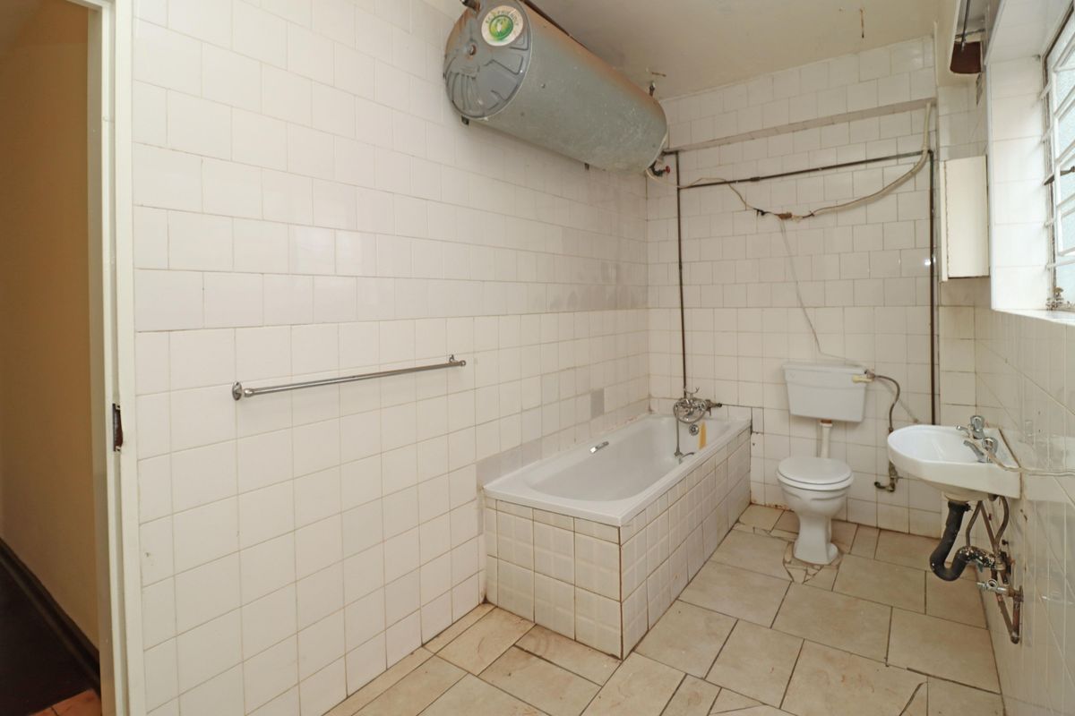 A dated bathroom featuring a built-in bathtub, toilet, and wall-mounted basin, requiring significant renovation and modernization of fixtures and finishes.