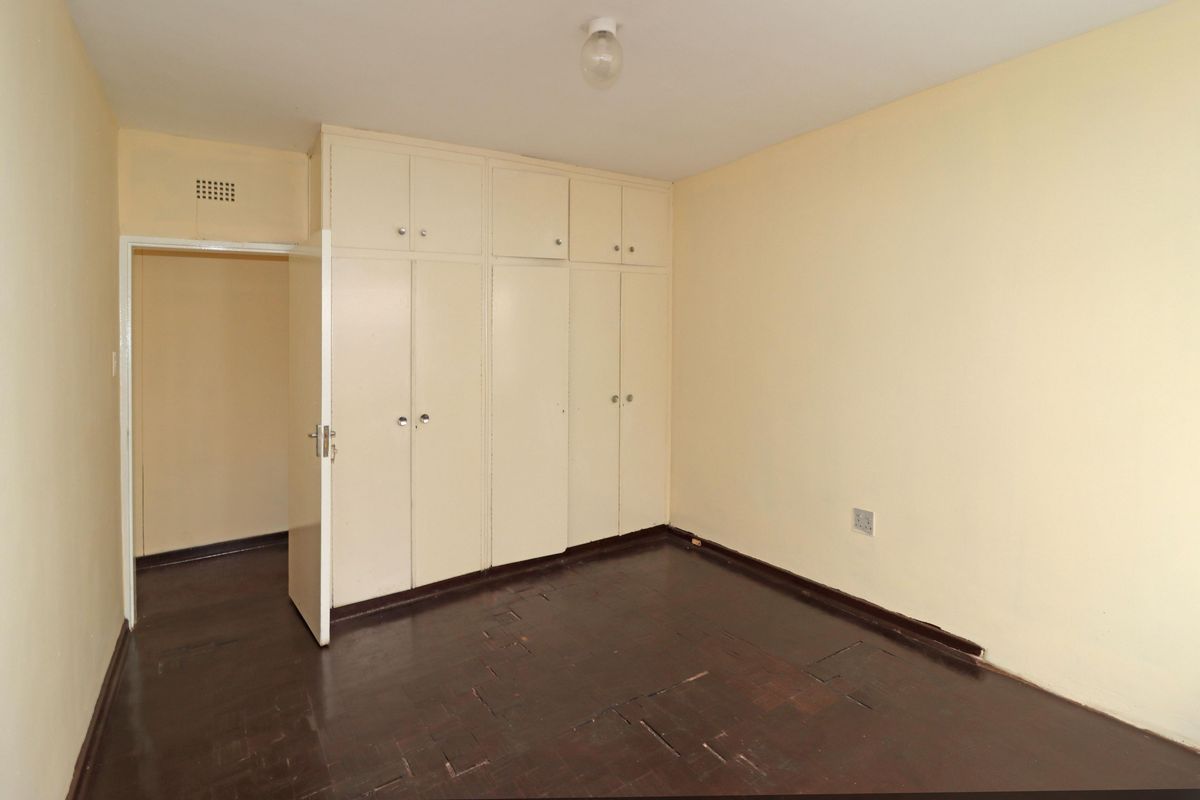A bedroom featuring built-in cupboards and dark parquet flooring, offering a blank canvas for renovation.