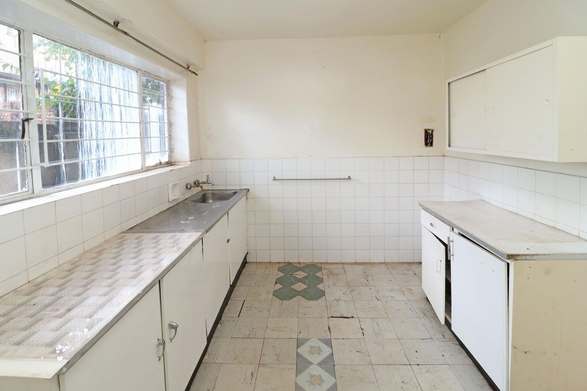 A dated kitchen featuring original cabinetry, a stainless steel sink, and tiled flooring, offering a blank canvas for a complete modern renovation.