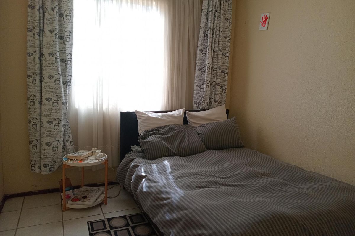 A bedroom featuring tiled flooring and a large window with curtains, providing natural light.