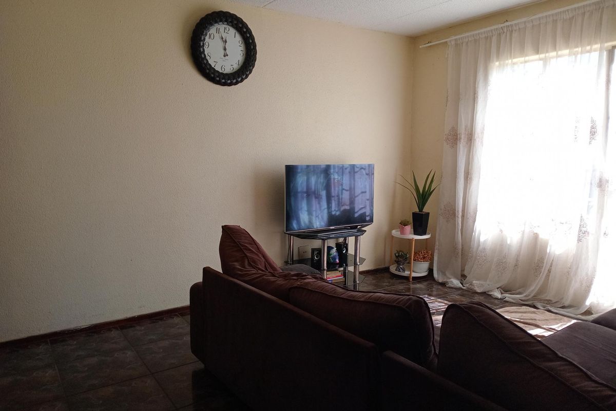 A living room featuring dark tiled flooring and natural light from a large window with sheer curtains.