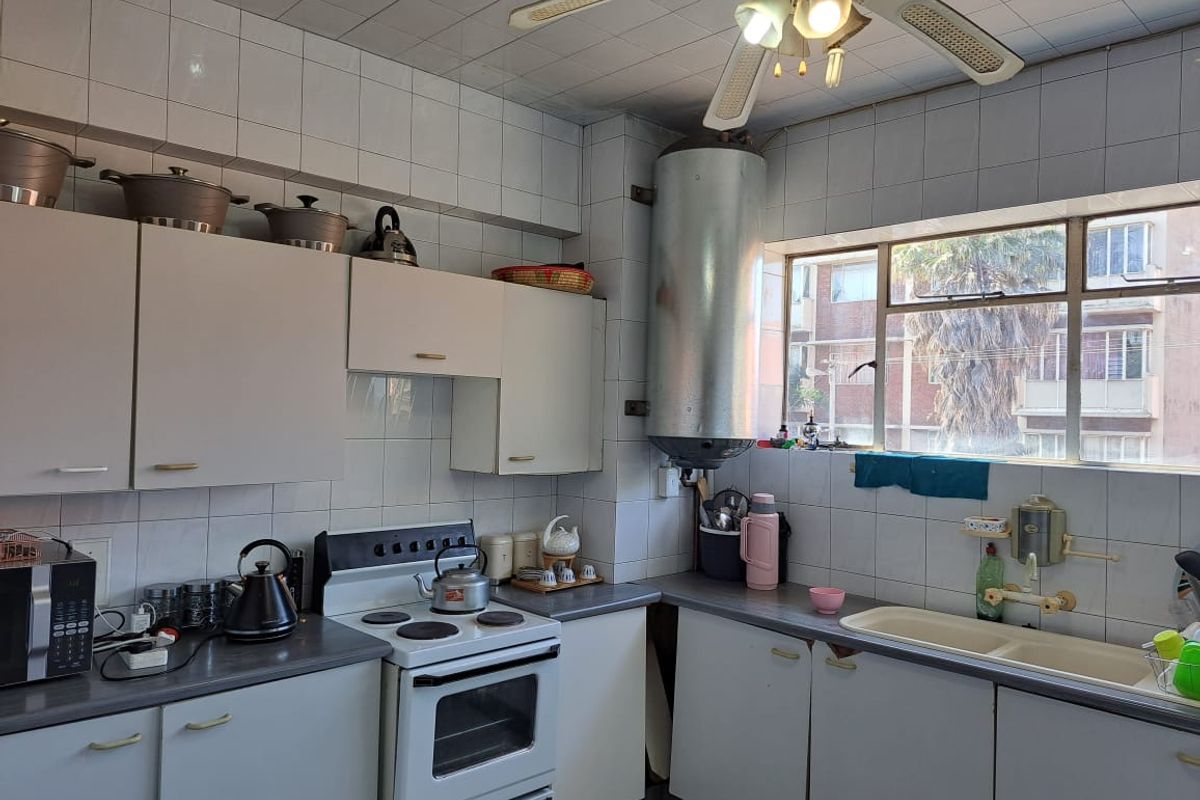 A functional kitchen featuring white cabinetry, a freestanding stove, a double basin sink, and a wall-mounted water heater cylinder.