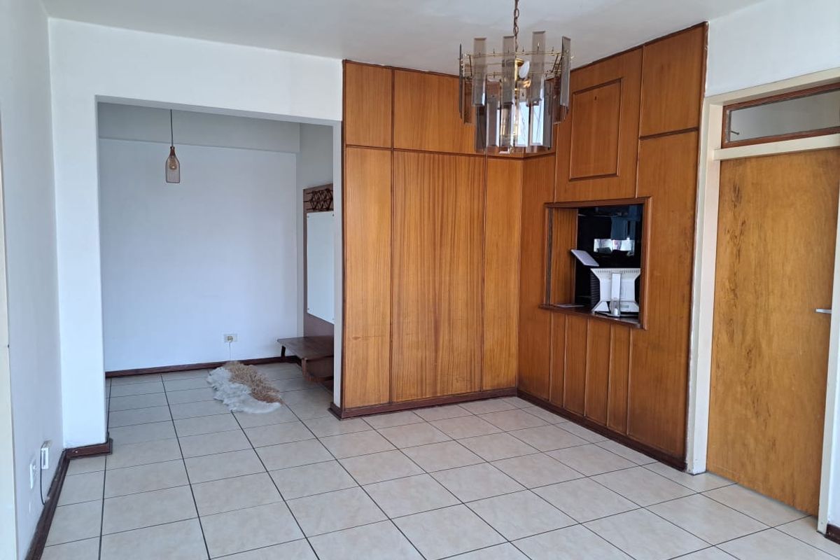 A spacious living area featuring classic wood wall paneling, ceramic floor tiles, and a built-in serving hatch connecting to the kitchen area.