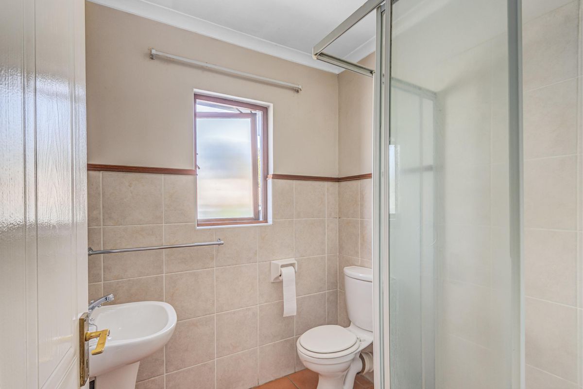 A functional bathroom featuring a pedestal basin, toilet, and a glass-enclosed shower with neutral wall and floor tiling.