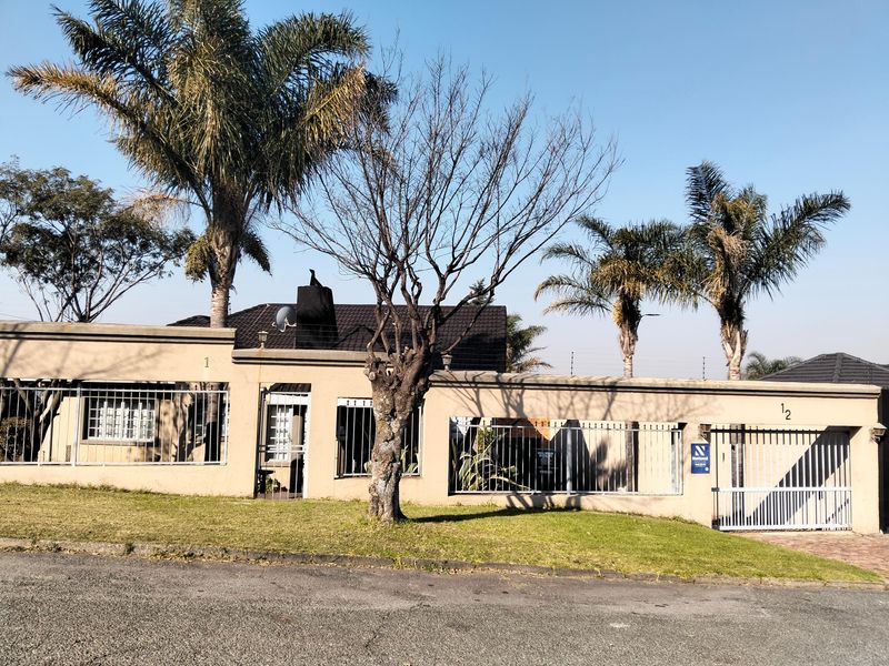 Front elevation of a residential property featuring a secure perimeter wall, gated entrance, and established landscaping.