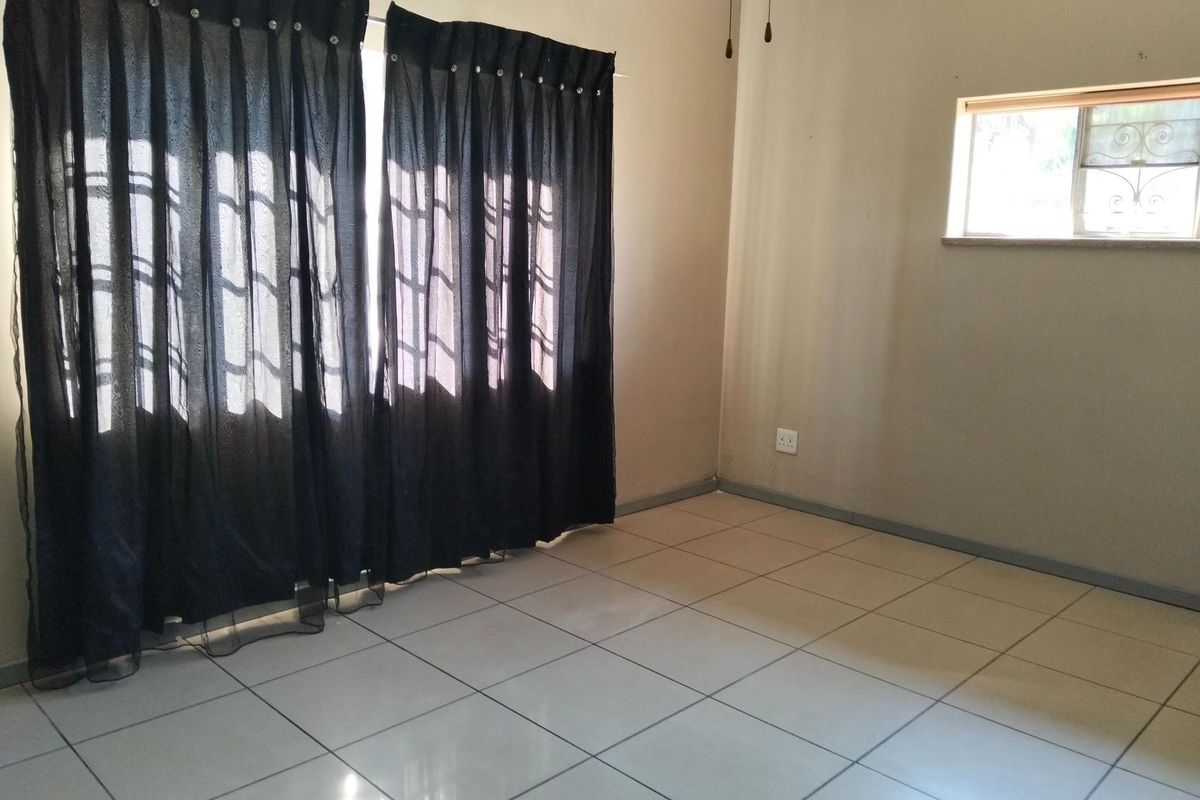 An empty bedroom featuring neutral wall paint, tiled flooring, and a window fitted with a security gate.