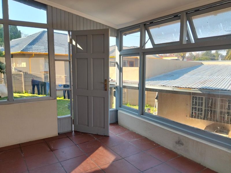 A sun-filled enclosed patio or sunroom featuring tiled flooring and extensive window glazing, offering a bright and versatile transition space.