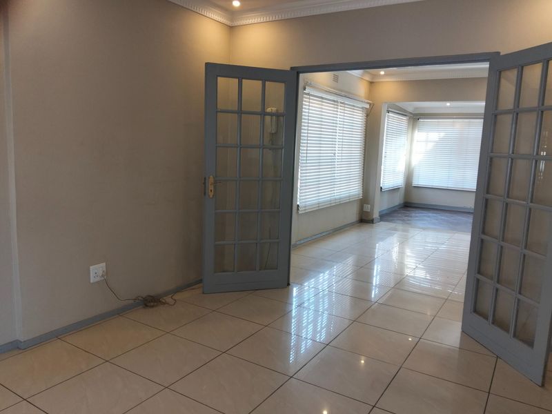 Spacious, light-filled living area featuring neutral tiled flooring, elegant french doors, and modern venetian blinds, offering a clean and versatile open-plan layout.