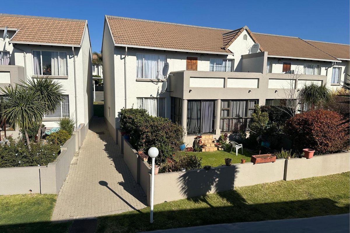 Exterior view of a residential apartment complex featuring tiled roofs, paved walkways, and private garden areas with established landscaping.