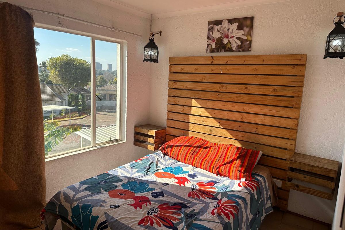 A bedroom featuring a large window with exterior views, textured walls, and tiled flooring.