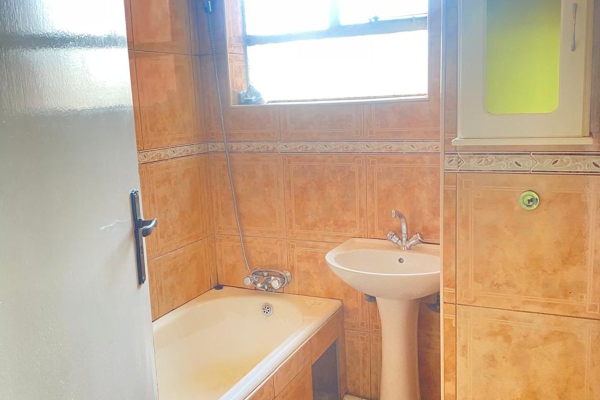 A dated bathroom featuring a built-in bathtub with shower mixer, pedestal basin, and full-height ceramic wall tiling.
