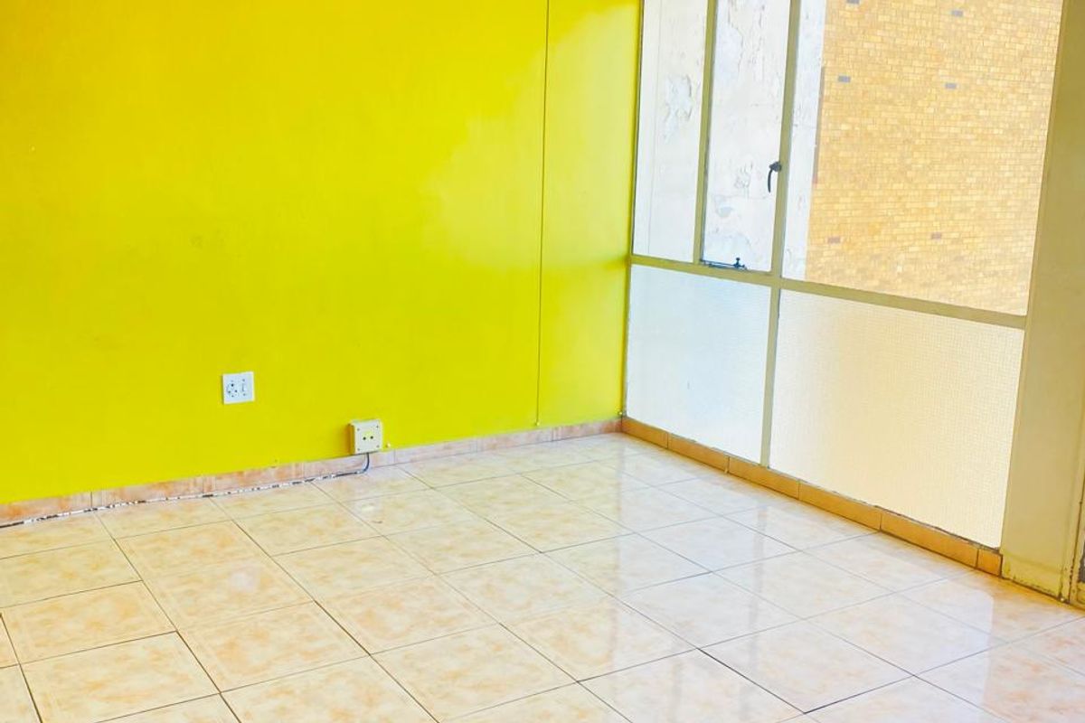 An empty living room featuring bright yellow walls, tiled flooring, and large floor-to-ceiling windows providing natural light.