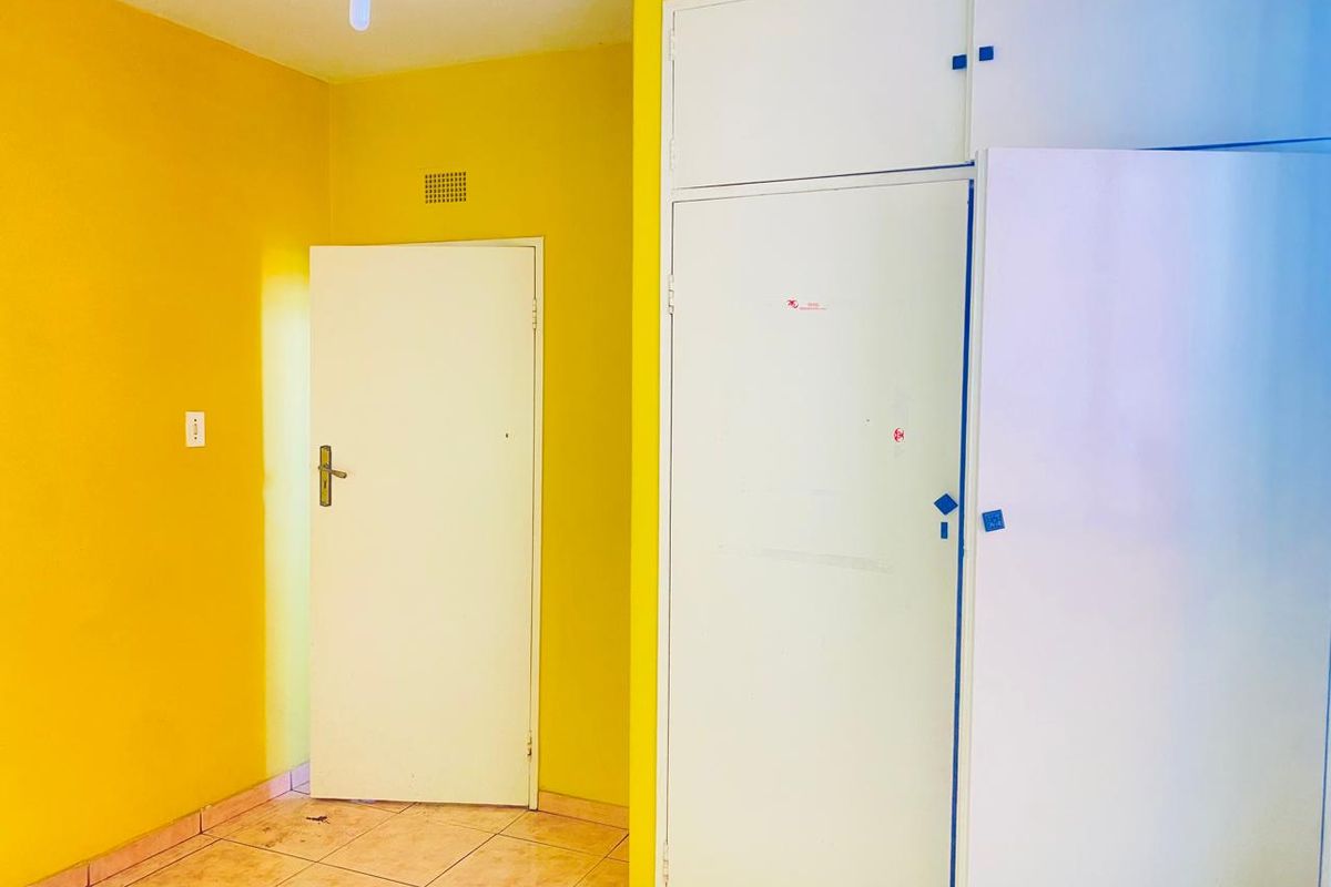 A bedroom interior featuring built-in cupboards, tiled flooring, and bright yellow wall paint.
