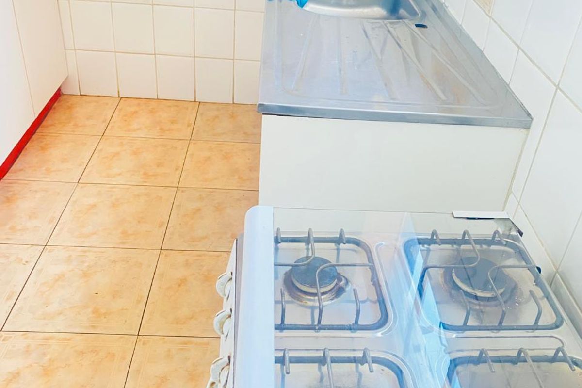 A functional kitchen area featuring a stainless steel double sink, tiled splashback, and a four-burner gas stove with a glass cover.