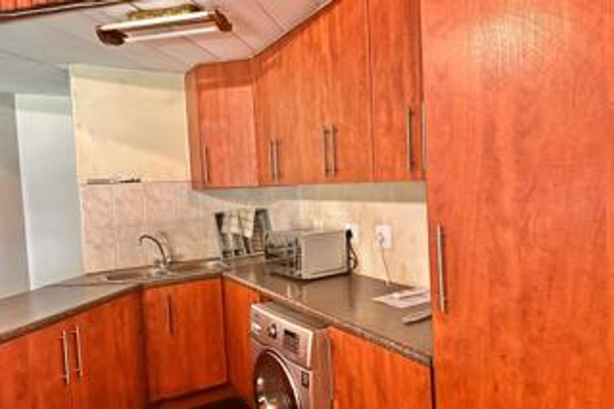 A functional kitchen featuring wood-tone cabinetry, laminate countertops, a stainless steel sink, and integrated laundry appliance space.