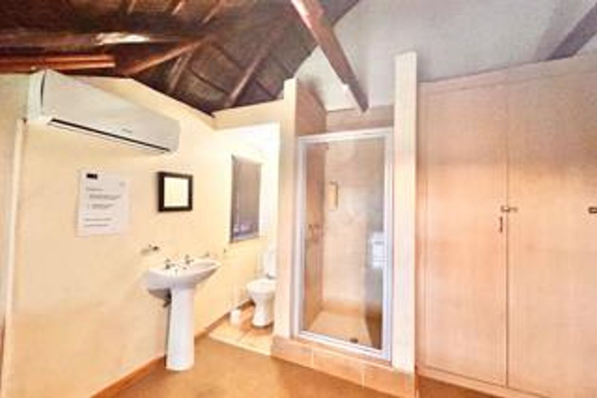 A functional bathroom featuring a pedestal basin, a glass-enclosed shower, a toilet, and built-in storage, complemented by a high vaulted ceiling.