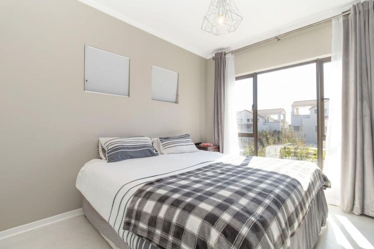 A bright bedroom featuring neutral wall tones, a large window with natural light, and modern pendant lighting.