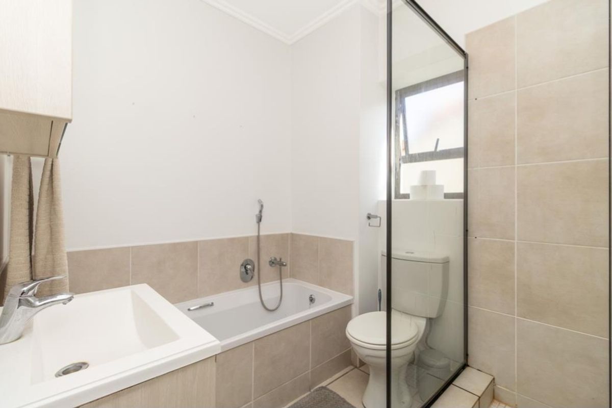 A functional bathroom featuring a built-in bathtub, a separate shower enclosure with a glass screen, and a vanity basin with storage.