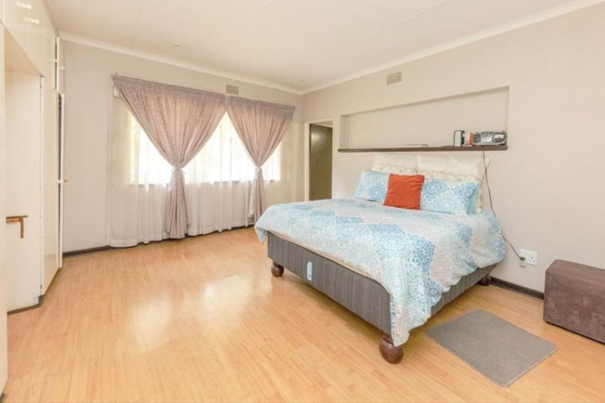 A spacious bedroom featuring light wood-look flooring, built-in cupboards, and a recessed wall niche above the bed area.