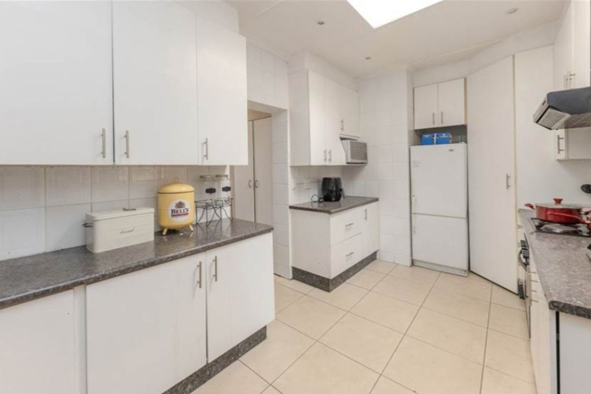 A functional kitchen featuring white cabinetry, stone-look laminate countertops, tiled flooring, and a built-in gas hob with an extractor fan.