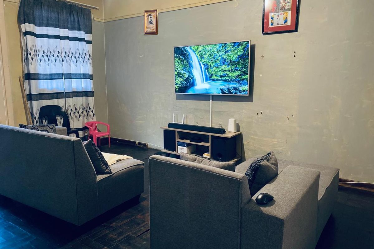 A living room featuring dark parquet flooring and a wall-mounted television, requiring cosmetic updates to the wall finishes.