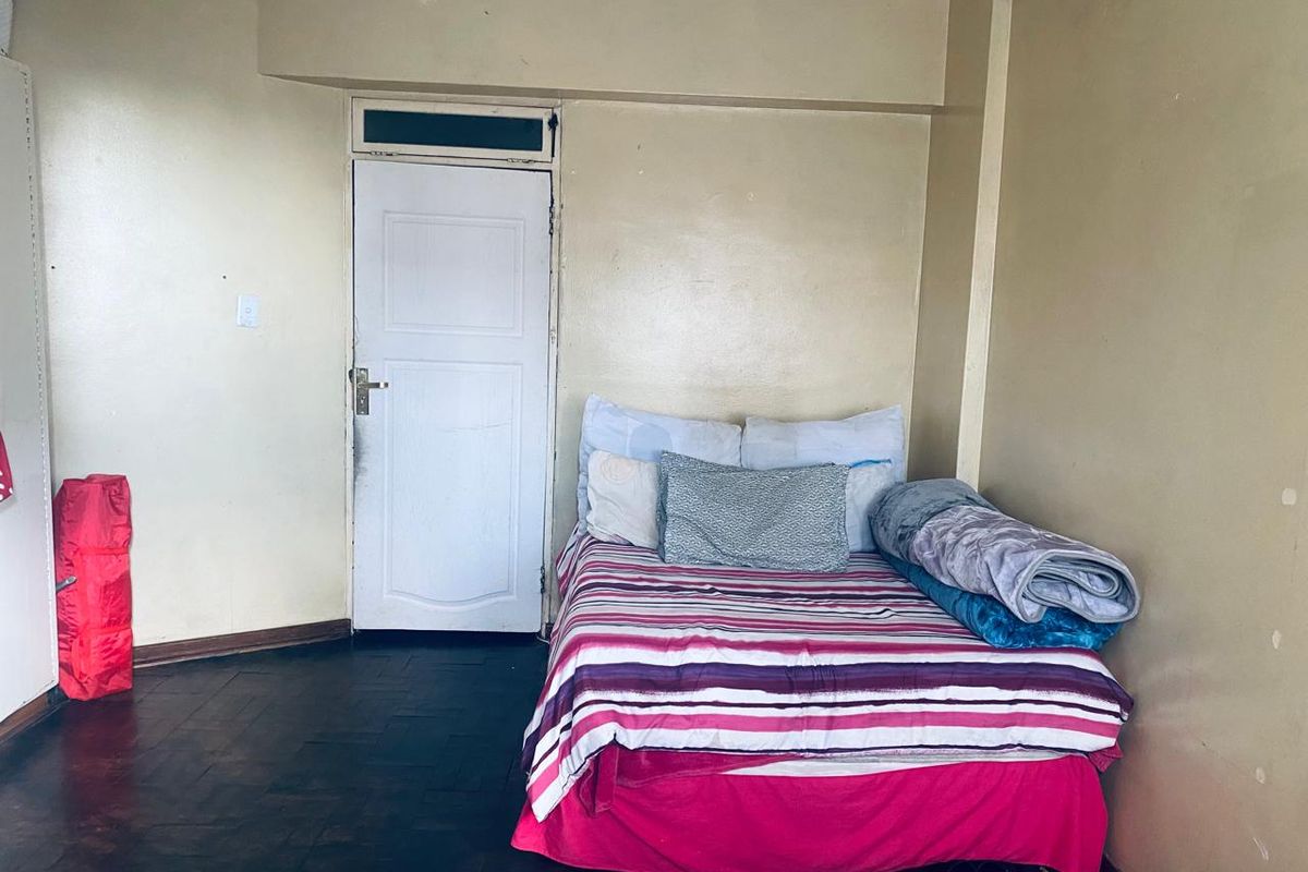 A bedroom featuring dark parquet flooring and a single door with a transom window, requiring cosmetic updates to improve the overall aesthetic.