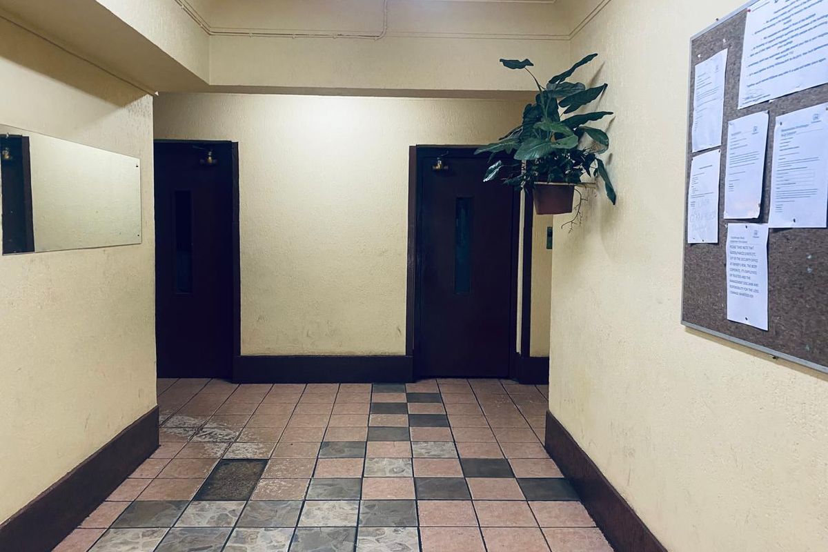 A communal hallway featuring tiled flooring, two dark wood doors, and wall-mounted notice board in a townhouse complex.