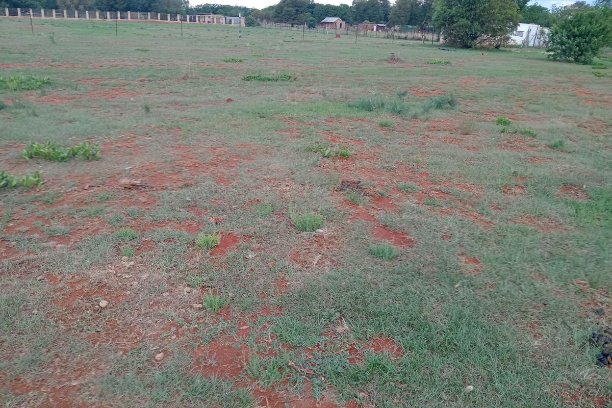A view of a vacant residential plot featuring open grass, red soil, and perimeter fencing, suitable for future development.