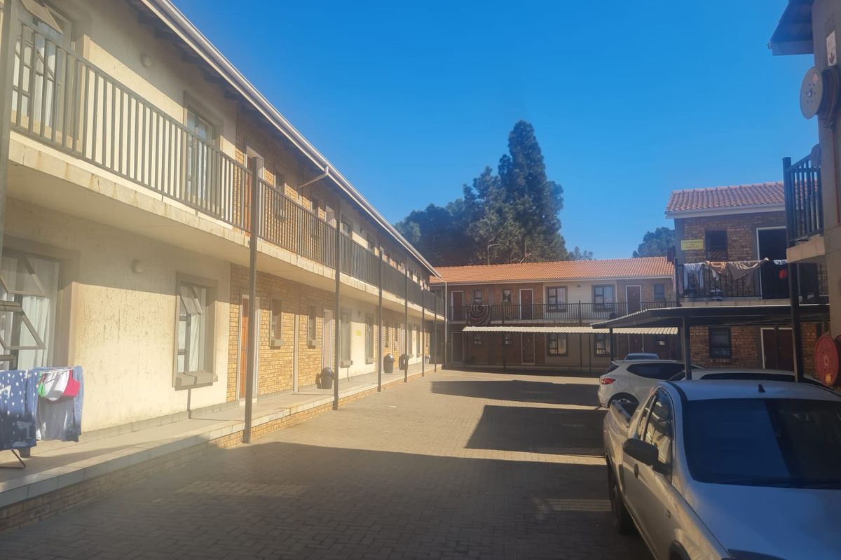 Exterior view of an apartment complex courtyard featuring paved parking areas, brick facade, and balcony access to upper-level units.