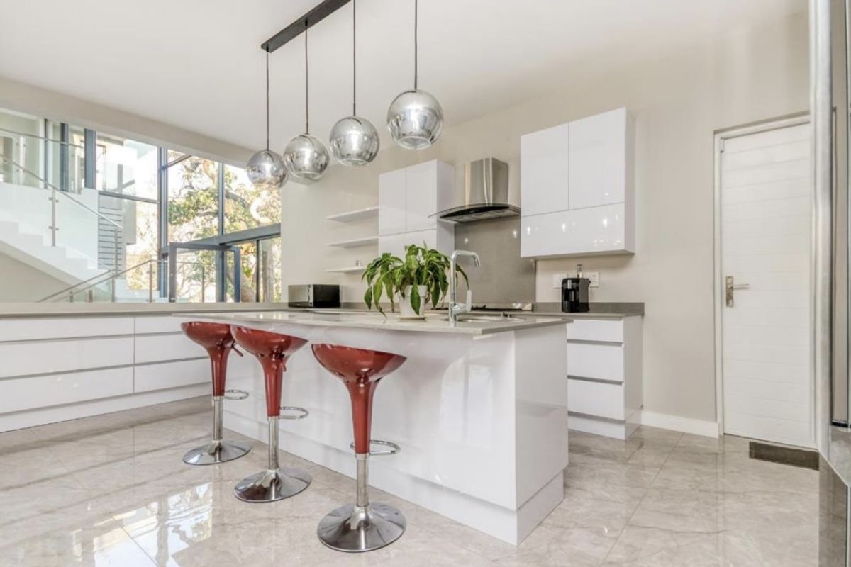 Modern kitchen featuring a central island with stone countertops, high-gloss cabinetry, stainless steel extractor fan, and contemporary pendant lighting.