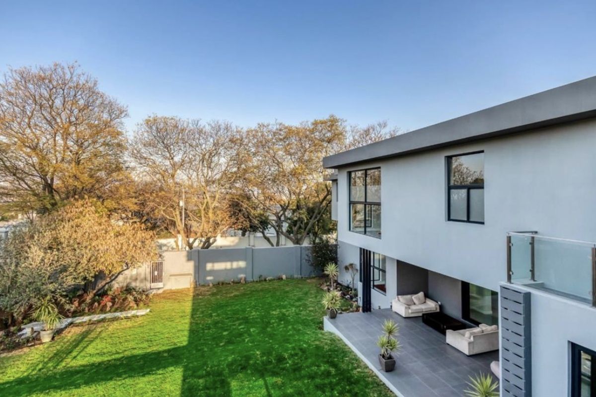 A view of the rear exterior of the modern house, featuring a tiled patio area, a well-maintained lawn, and a perimeter boundary wall.