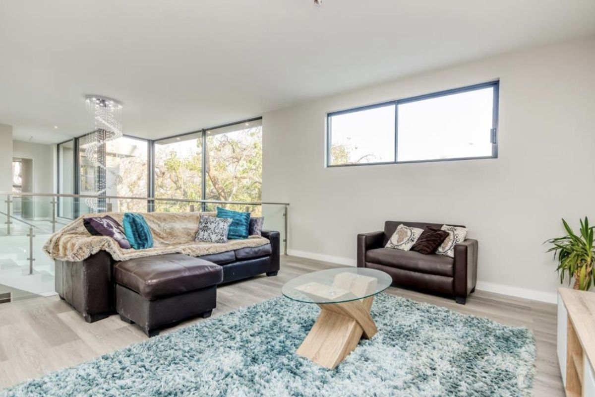 Spacious living area featuring large floor-to-ceiling windows, modern glass balustrades, and light-toned wood-look flooring.