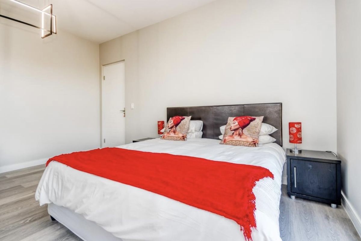 A well-maintained bedroom featuring modern laminate flooring, neutral wall finishes, and a contemporary pendant light fixture.