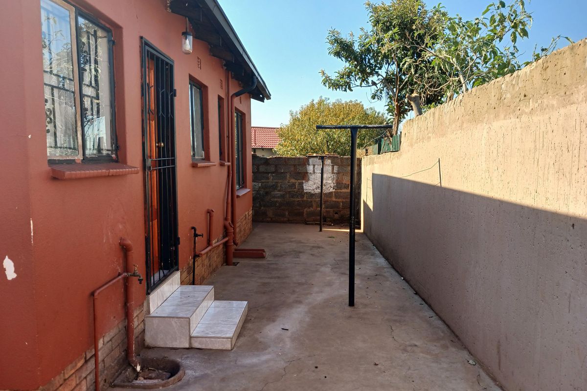 A side exterior view of the property featuring a concrete pathway, security gate, and perimeter boundary wall.
