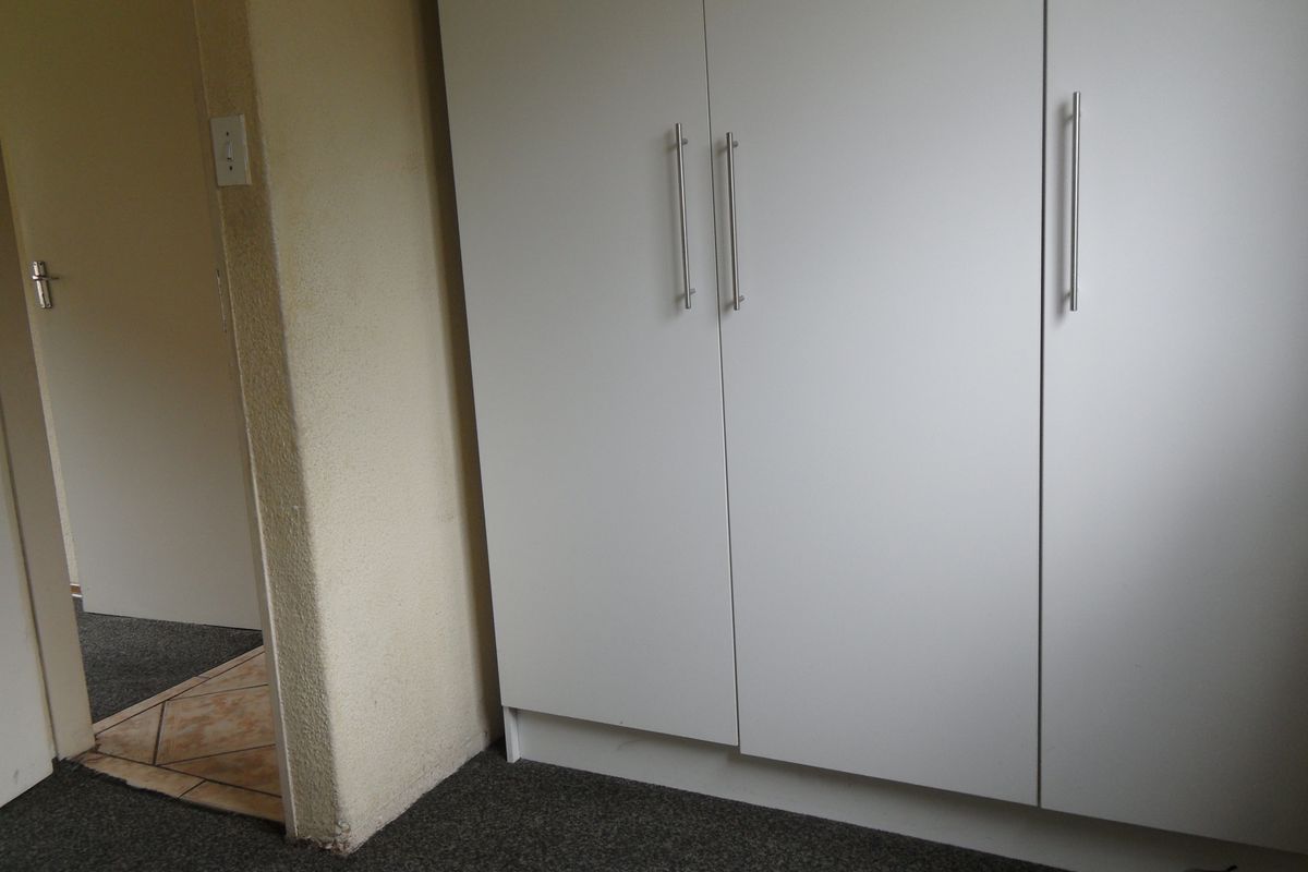 A bedroom interior featuring built-in white cabinetry with modern handles and carpeted flooring, leading into an adjacent tiled hallway.