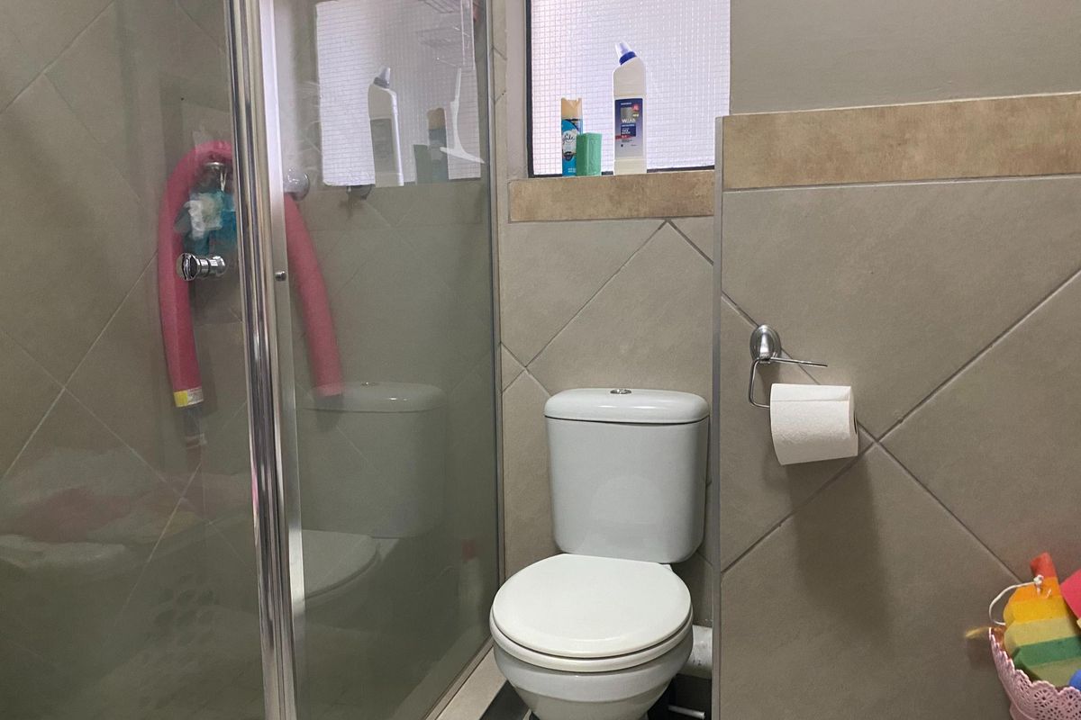 A functional bathroom featuring a glass-enclosed shower, a standard toilet, and neutral wall tiling with a small frosted window.