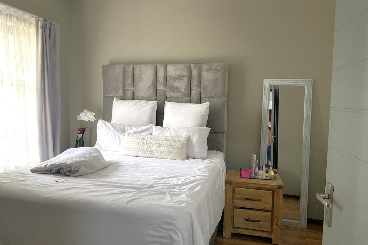 A well-maintained bedroom featuring neutral wall tones, laminate flooring, and a large window allowing natural light.