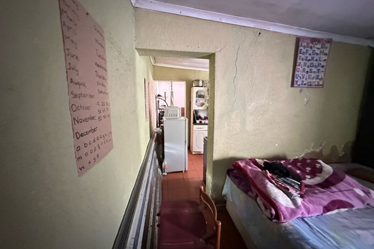 A bedroom space showing significant wear, including cracked plaster and signs of damp damage on the lower wall sections.